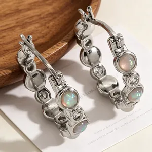 Close-up detail of silver hoop earrings with opal and zircon stones on a wooden tray.