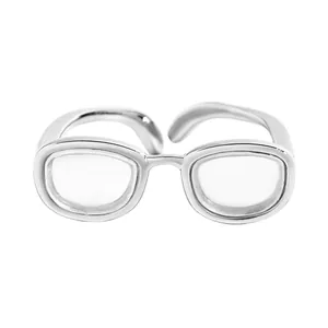 Gros plan d'une bague réglable argentée créative au design de monture de lunettes miniature.