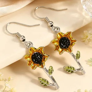 Detailaufnahme von leuchtend gelben Emaille-Sonnenblumen-Ohrhängern mit grünen Blättern