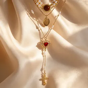 Macro shot of layered gold necklace featuring a red heart stone and crucifix pendant.