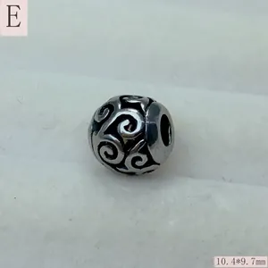 Close-up view of a retro hollow stainless steel filigree charm bead with scroll patterns
