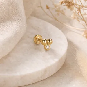 Dettaglio macro di un piercing 16G in argento S925 con palline dorate e zircone