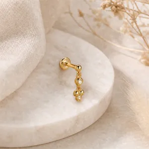 Dettaglio macro di un piercing lobo in argento S925 placcato oro 16G con zirconi.