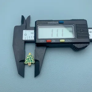 Gros plan d'une breloque sapin de Noël en émail vert mesurée avec un pied à coulisse numérique