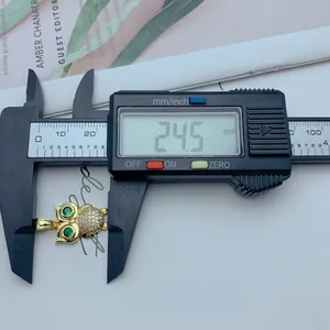 Primer plano de un colgante de búho dorado con ojos de circón verde medido por un calibre