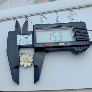 Primer plano de un dije de margarita de esmalte blanco medido a 15,3 mm con un calibre.