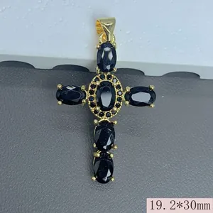 Detalle de colgante de cruz bañada en oro con circonitas negras ovales y brillo