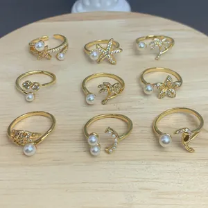 Set mit neun goldfarbenen verstellbaren Ringen mit Perlen und Zirkonia auf Holz