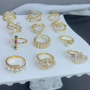 Vista detallada de anillos de oro con perlas y circonitas, diseños de corazón y mamá