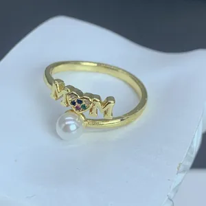 Detalle de un anillo MOM dorado con una perla blanca y corazón de circonitas de colores