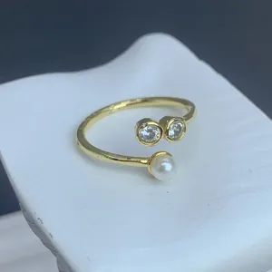 Detailansicht eines verstellbaren goldfarbenen Rings mit zwei Zirkonia und Perle.