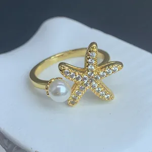 Nahaufnahme eines goldenen Seestern-Rings mit Zirkonia-Besatz und einer weißen Perle