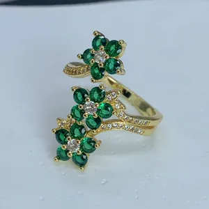 Vista detallada de un anillo abierto dorado con flores de circonita verde y clara.