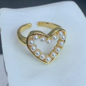 Vista detallada de un anillo abierto dorado con un diseño de corazón con perlas