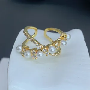 Vista detallada de un elegante anillo cruzado de oro con perlas y circonitas.