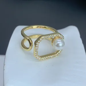 Primer plano de un anillo geométrico dorado con una perla blanca y circonitas.