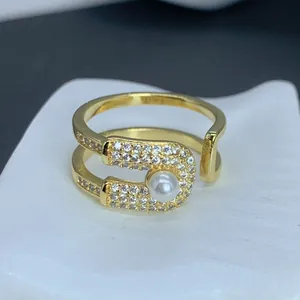 Detalle macro de un anillo de imperdible dorado con perla y detalles de circonita.