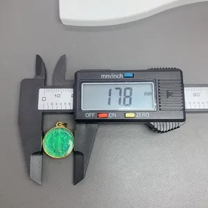 Primer plano del colgante San Benito de esmalte verde midiendo 17,8 mm con calibre.