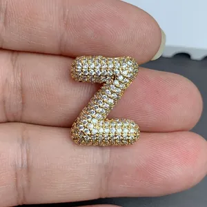 Gros plan d'un pendentif lettre Z doré pavé de pierres étincelantes entre les doigts