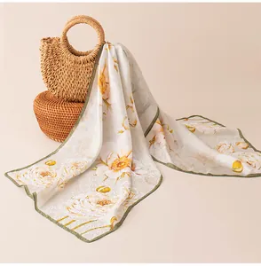Detail view of a luxury floral print mulberry silk scarf draped over a woven straw bag.
