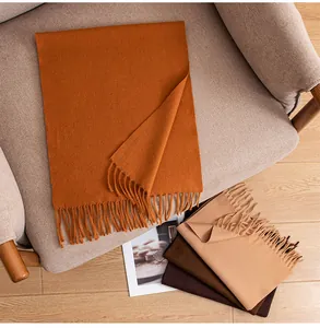 Cozy winter wool scarves with fringes displayed on a beige armchair in a warm room.