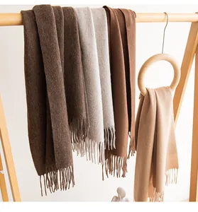 Multiple solid color wool scarves with fringe displayed on a minimalist wooden rack