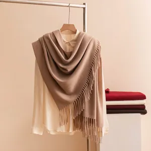 Detail view of a brown wool scarf with fringe draped on a hanger in a studio setting.