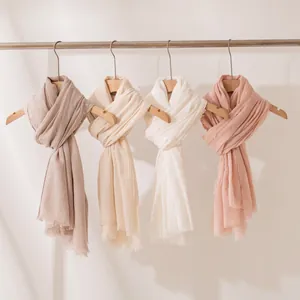 Selezione di scialli leggeri in misto lana in tenui colori pastello su grucce di legno.
