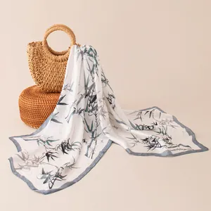 Elegant white silk scarf with traditional bamboo print draped over a straw bag