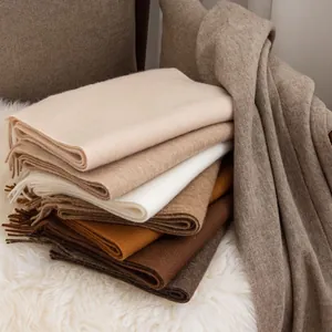 Close-up detailed view of stacked warm wool scarves in neutral earthy tones with soft fringe