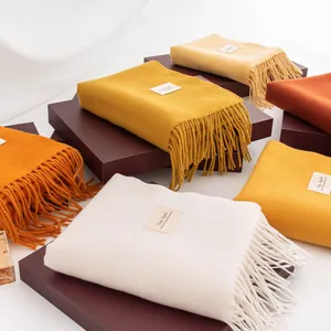 Detail view of assorted Morandi color fringe scarves stacked on gift boxes