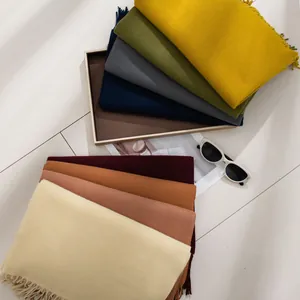 Assorted solid color winter scarves with fringe details displayed on a clean white surface.