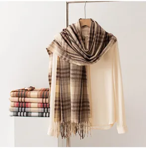 Close-up view of a thick checkered scarf with fringe draped over a beige shirt on a rack