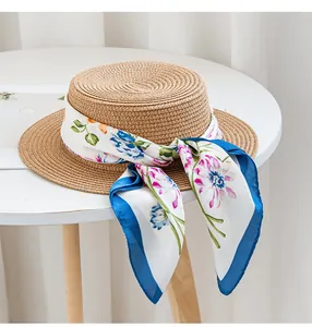 Detail showing a colorful floral silk scarf elegantly tied around a straw boater hat on a table.
