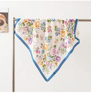 Detail of a lightweight floral silk scarf with blue border hanging on a metal rack.