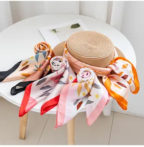 Detail of elegant floral print silk scarves and a straw hat on a clean white table