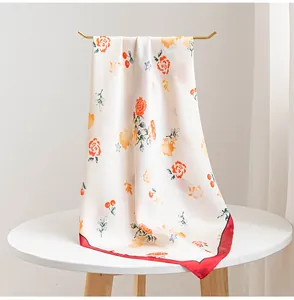 Dettaglio di un foulard in seta leggero con rose arancioni e bordo rosso vivace