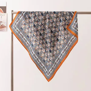 Détail rapproché d'un foulard en soie imprimé floral vintage avec une bordure orange vive.
