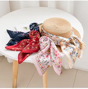 Vista dettagliata di foulard in seta a fiori colorati e un cappello di paglia su un tavolo.