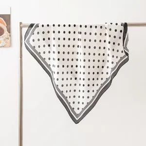 Elegant white silk scarf with black polka dots draped over a metal rod for display
