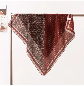 Dettaglio di un foulard in seta bordeaux con motivi paisley e pois su un supporto