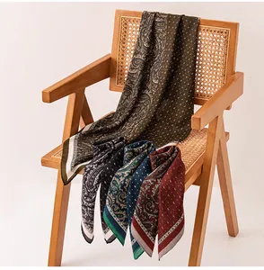 Dettaglio di sciarpe quadrate in seta con stampe paisley e pois disposte su una sedia.