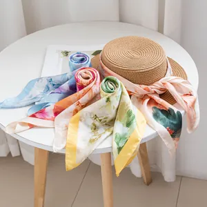 Elegant floral silk neck scarves displayed with a straw hat on a white round table.
