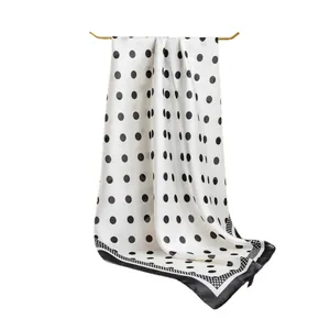 Elegant white silk scarf with black polka dots draped on a gold metal hanger bar.