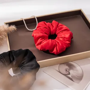 Close-up detail of luxurious red silk satin scrunchie with elegant pleated texture