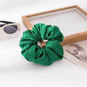 Macro view of a vibrant green satin scrunchie showing its luxurious silk-like texture