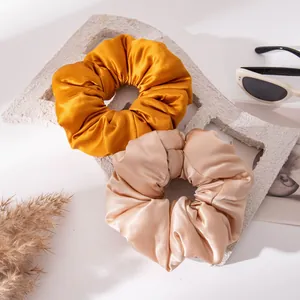 Two luxurious silk satin hair scrunchies in mustard and champagne pink on stylish props.