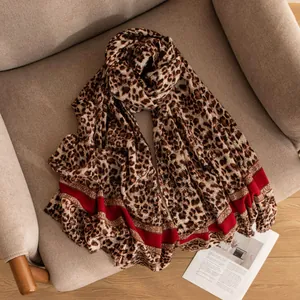 Elegante sciarpa in lana sottile con stampa leopardata e bordo rosso su una poltrona beige.