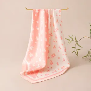 Detail view of elegant pink floral silk square scarf draped on a minimalist gold hanger