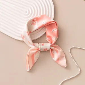 Elegant pink floral silk scarf detail with pearl accessory in warm beige setting.